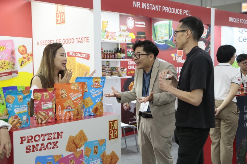 Participants speak at the Fancy Food Show near a booth that says Protein Snack